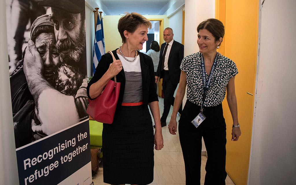La conseillère fédérale Simonetta Sommaruga et la directrice de l’autorité grecque de l’asile Maria Stavropoulou. À gauche, une affiche représentant des réfugiés, avec le slogan 