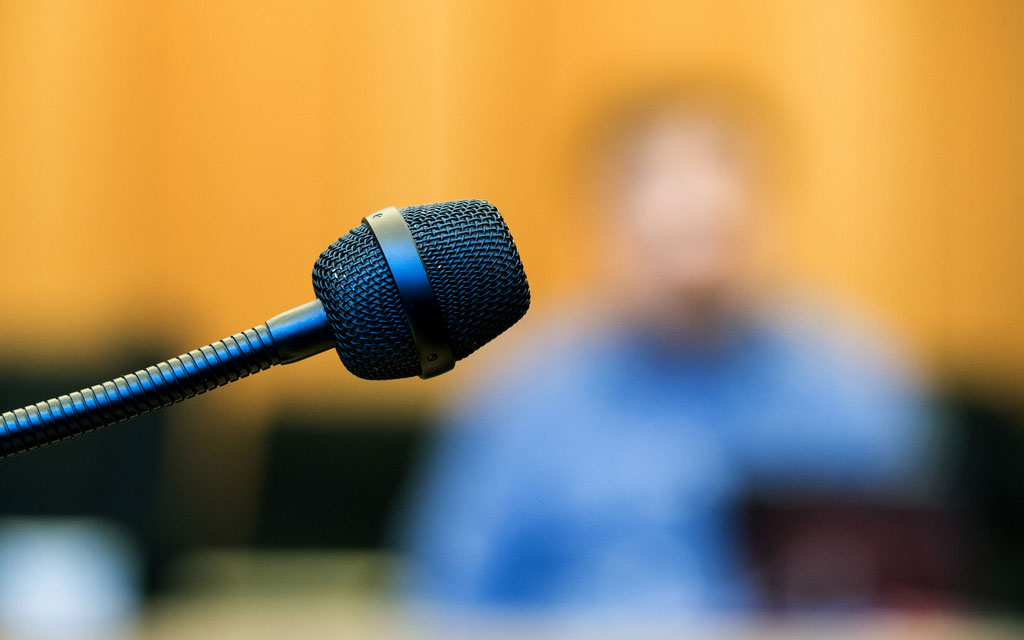 Visage flouté d’un témoin derrière le microphone dans la salle d’audience